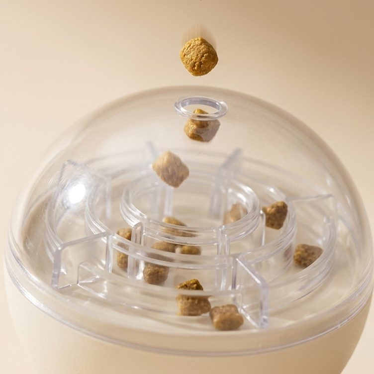 Une croquette tombe dans l'orifice de remplissage au sommet du dôme transparent du jouet Naïa Malin