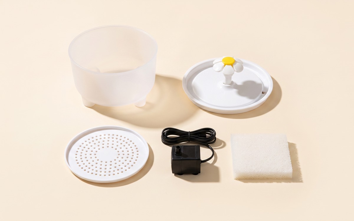Pièces de la fontaine Naïa démontées pour le nettoyage : cuve, plateau à fleur, grille, pompe et mousse filtrante carrée